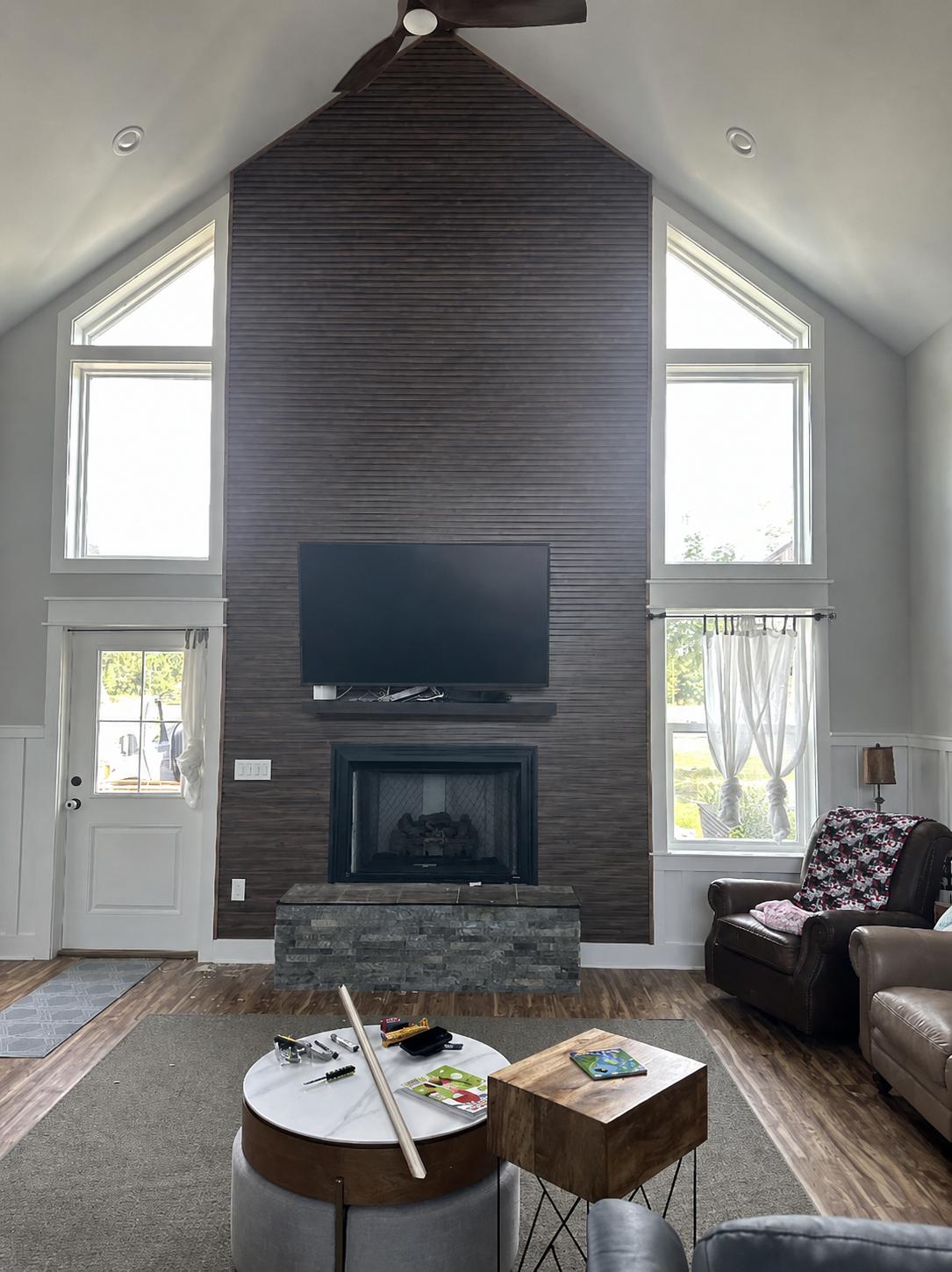 Sala de doble altura con panel de lamas de madera, TV y chimenea de piedra